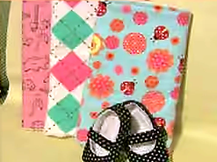 Quilted burp cloths in bright cotton prints, stacked with a pair of baby shoes.