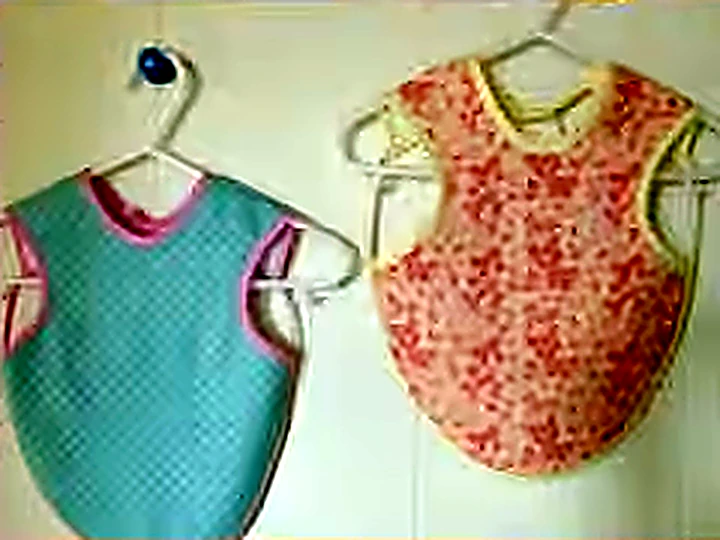 Two reversible baby bibs hanging on wooden hangers.